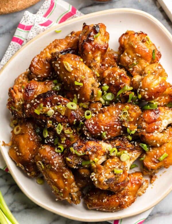 honey garlic chicken wings on a plate topped with green onions and sesame seeds