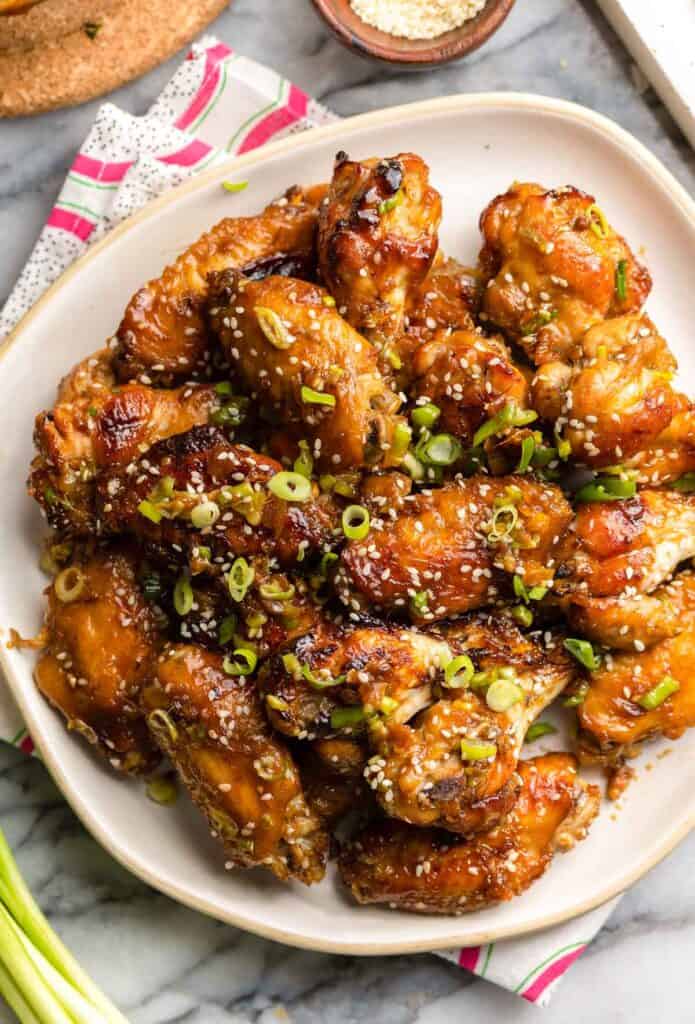 a plate of honey garlic chicken wings with green onions and sesame seeds