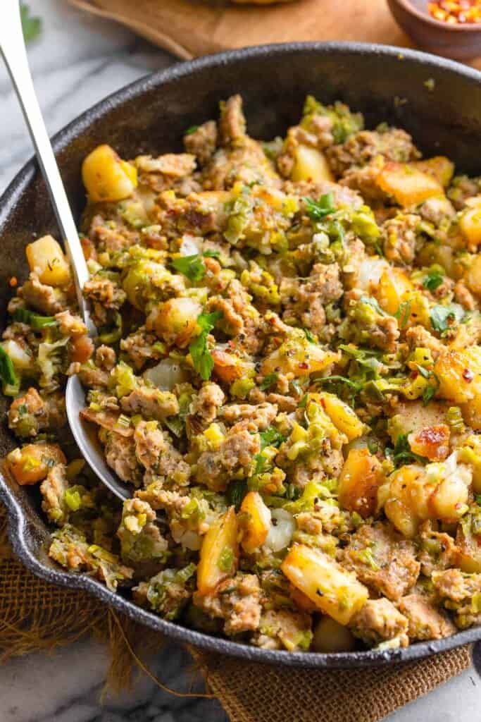 a skillet full of a Potato & Leek Turkey Hash with a spoon in it