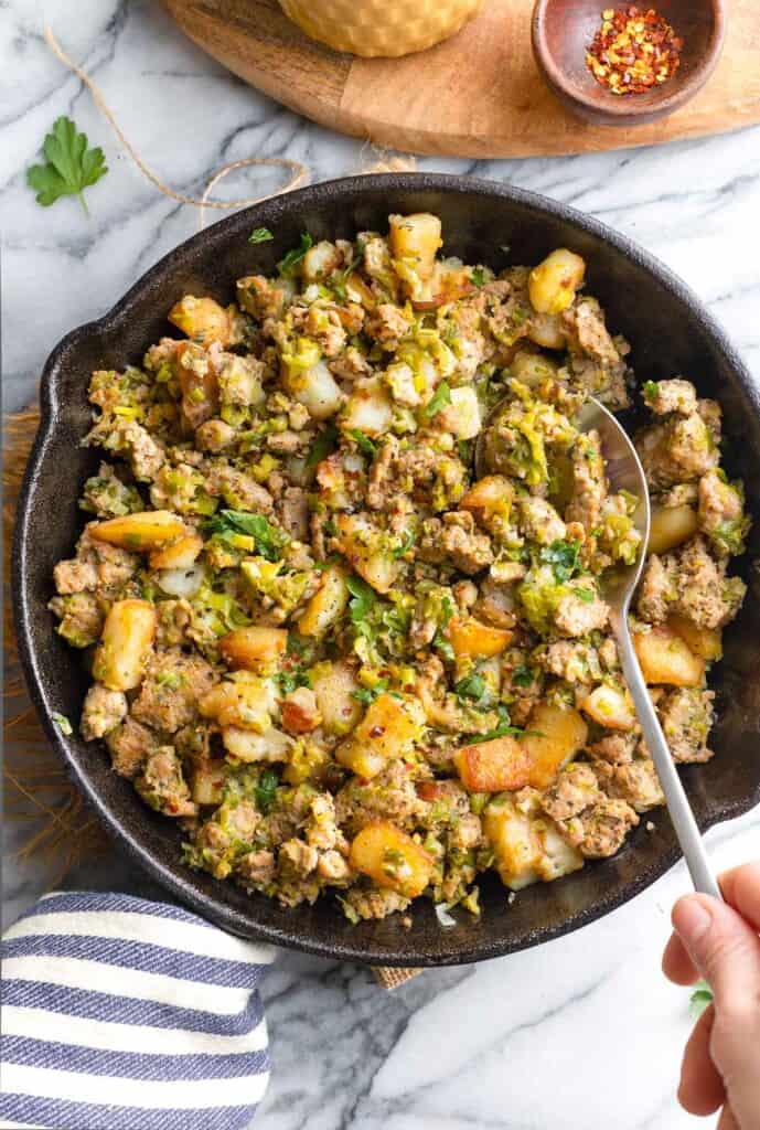Potato & Leek Turkey Hash in a cast iron skillet with a serving spoon scooping out a portion