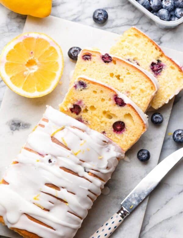 gluten free blueberry loaf cake sliced and surrounded by fresh lemons and berries