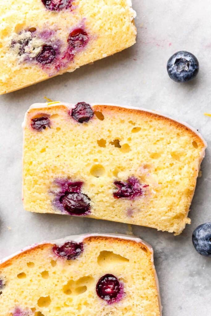 slices of Gluten Free Blueberry Lemon Loaf laying flat on a marble surface surrounded by blueberries