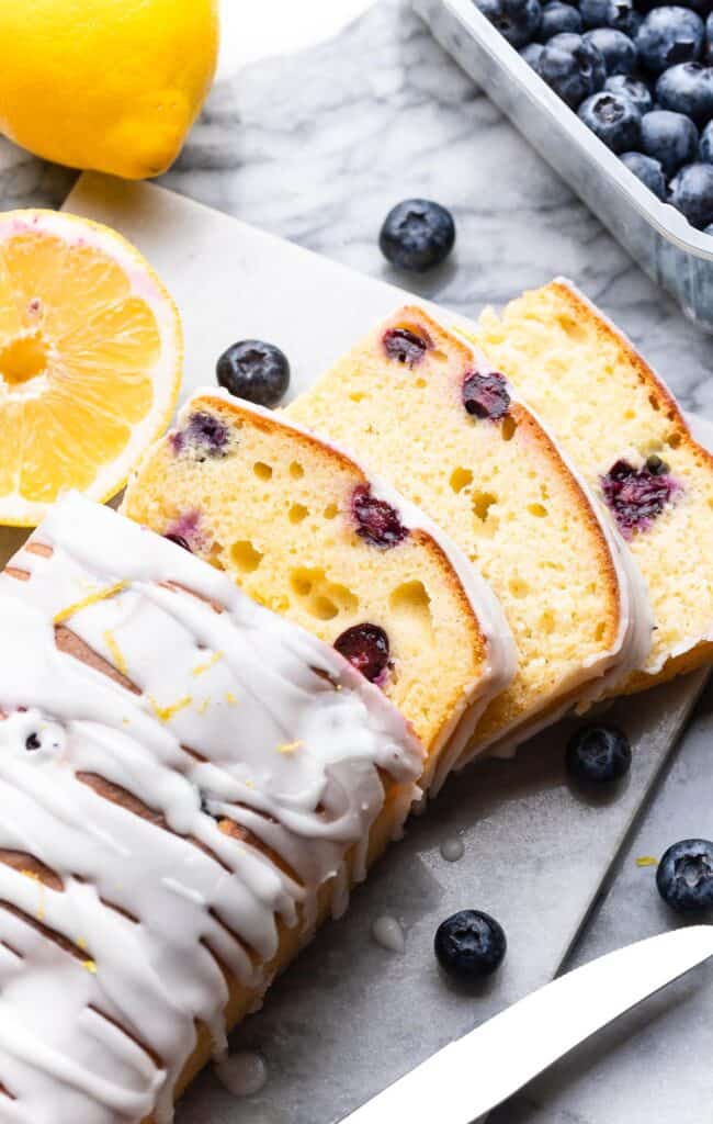 a sliced gluten free Blueberry Lemon Loaf with fresh blueberries and lemons on the side