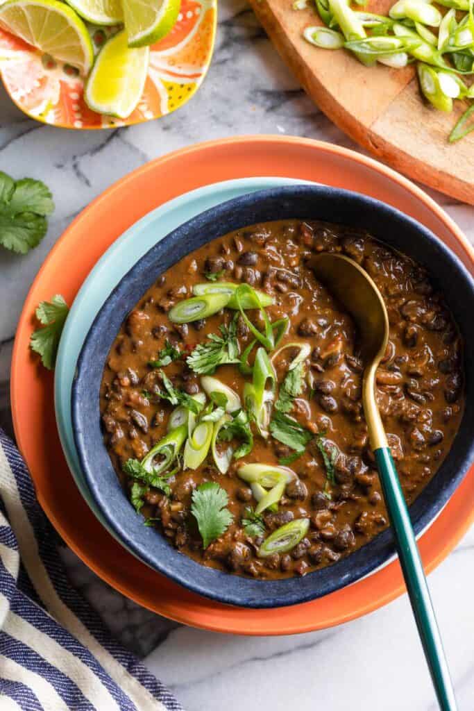 sautéd black beans in a serving bowl with a spoon topped with fresh garnishes 