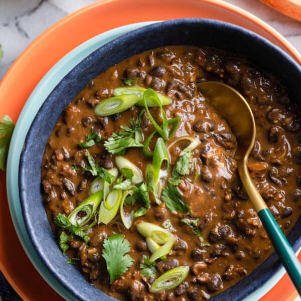 adobo black beans in a serving bowl with a spoon topped with fresh cilantro and spring onions