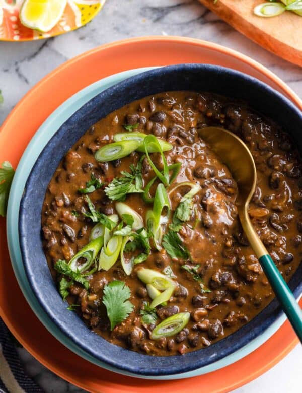 adobo black beans in a serving bowl with a spoon topped with fresh cilantro and spring onions