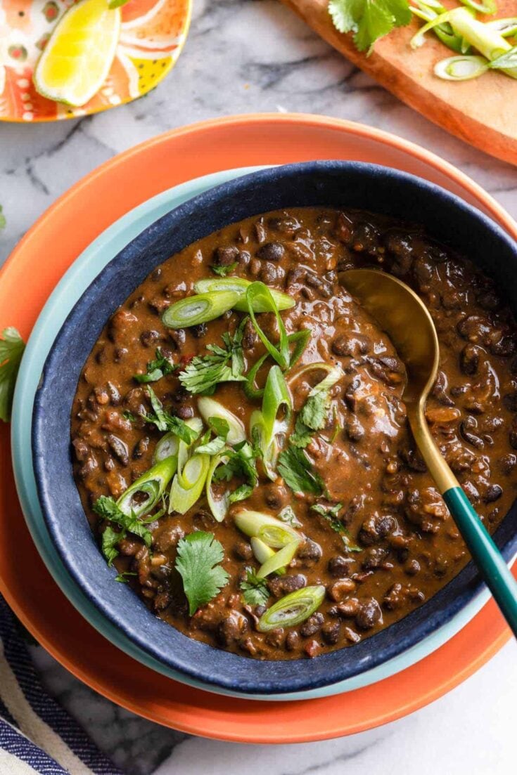 adobo black beans in a serving bowl with a spoon topped with fresh cilantro and spring onions