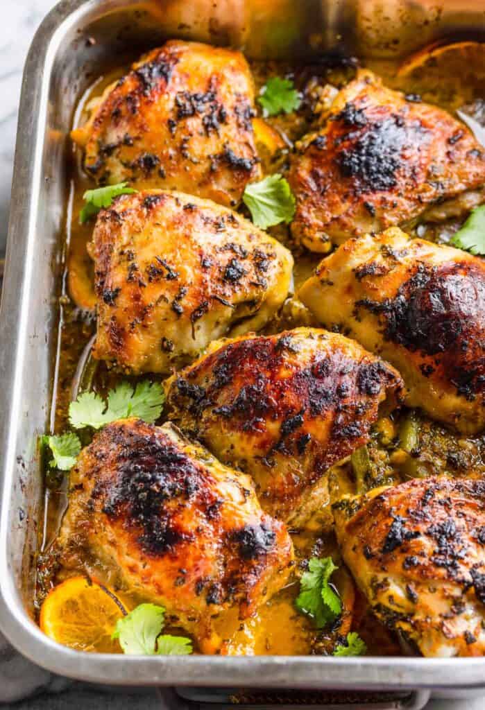 seven, cooked mojo marinated chicken thighs over sliced peppers and oranges in a baking dish topped with fresh cilantro