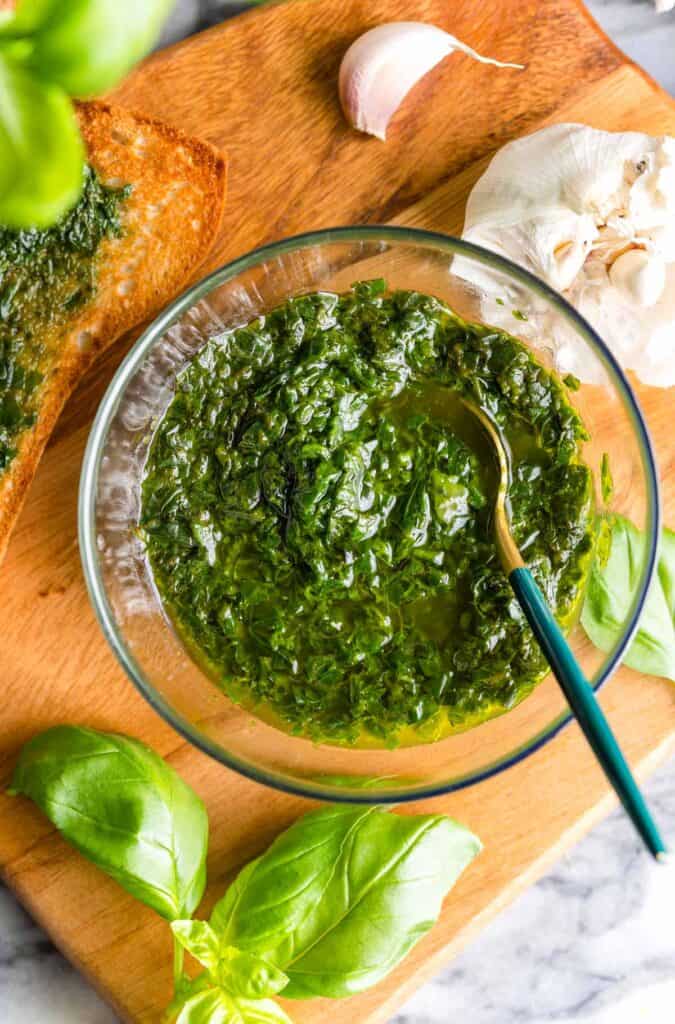 pistou sauce in a serving bowl with a spoon surrounded by fresh basil and garlic