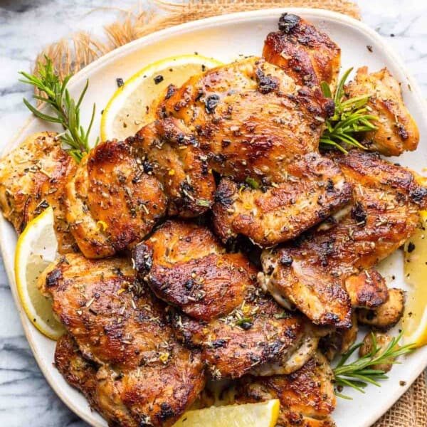 Greek Marinated Chicken on a plate with lemon slices and fresh rosemary sprigs