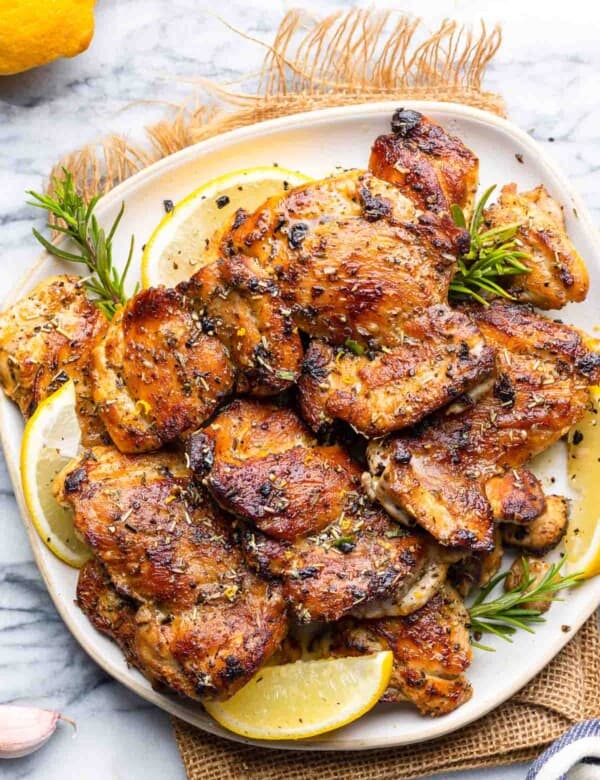 Greek Marinated Chicken on a plate with lemon slices and fresh rosemary sprigs