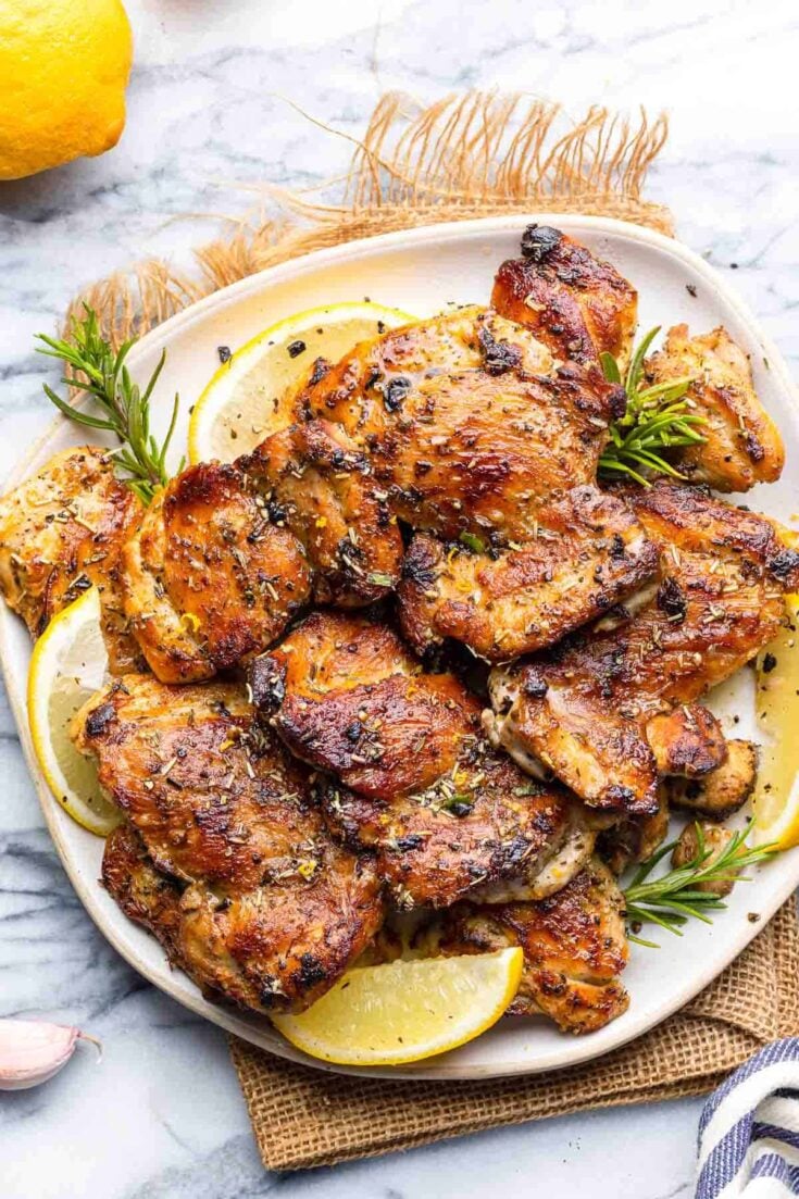 Greek Marinated Chicken on a plate with lemon slices and fresh rosemary sprigs