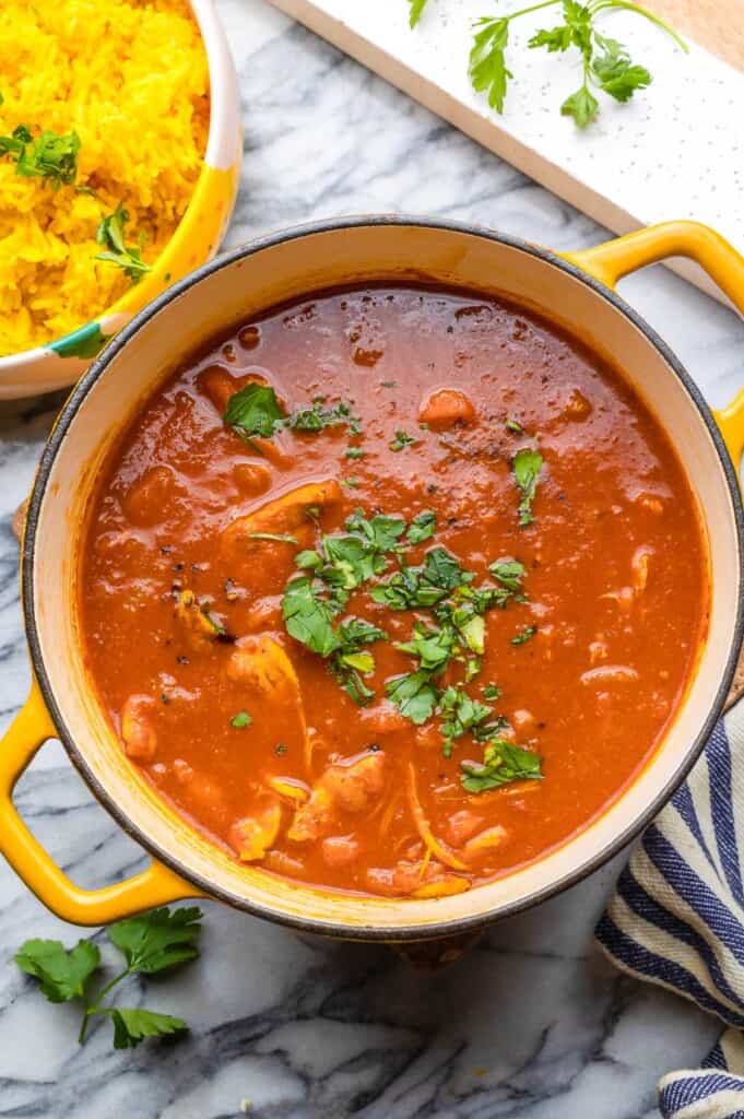 Moroccan Chicken Stew in a big pot with fresh parsley sprinkled on top and curried rice in the corner