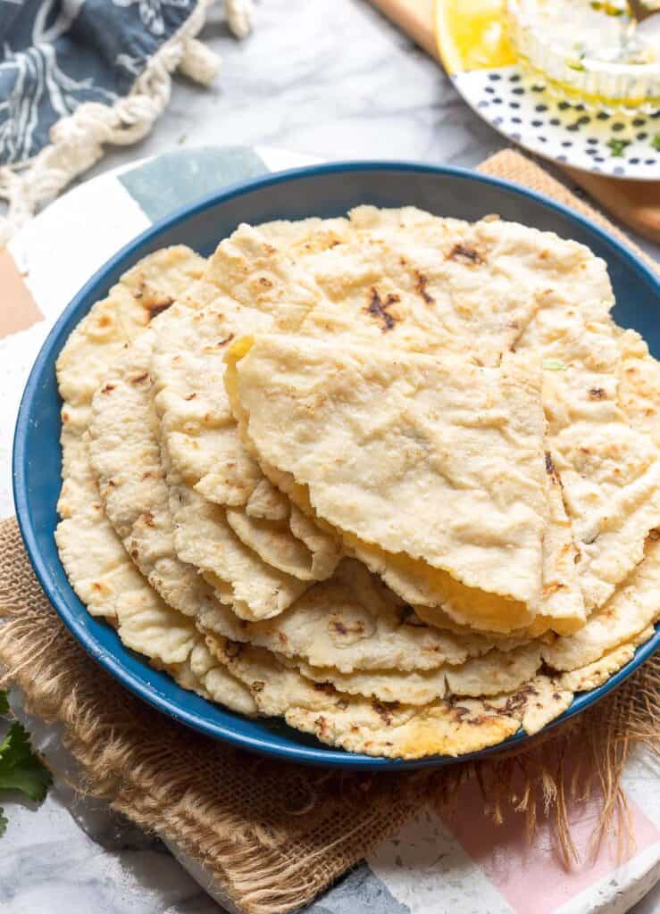 a stack of gluten free roti on a plate with the top roti folded up to demonstrate how flexible it is