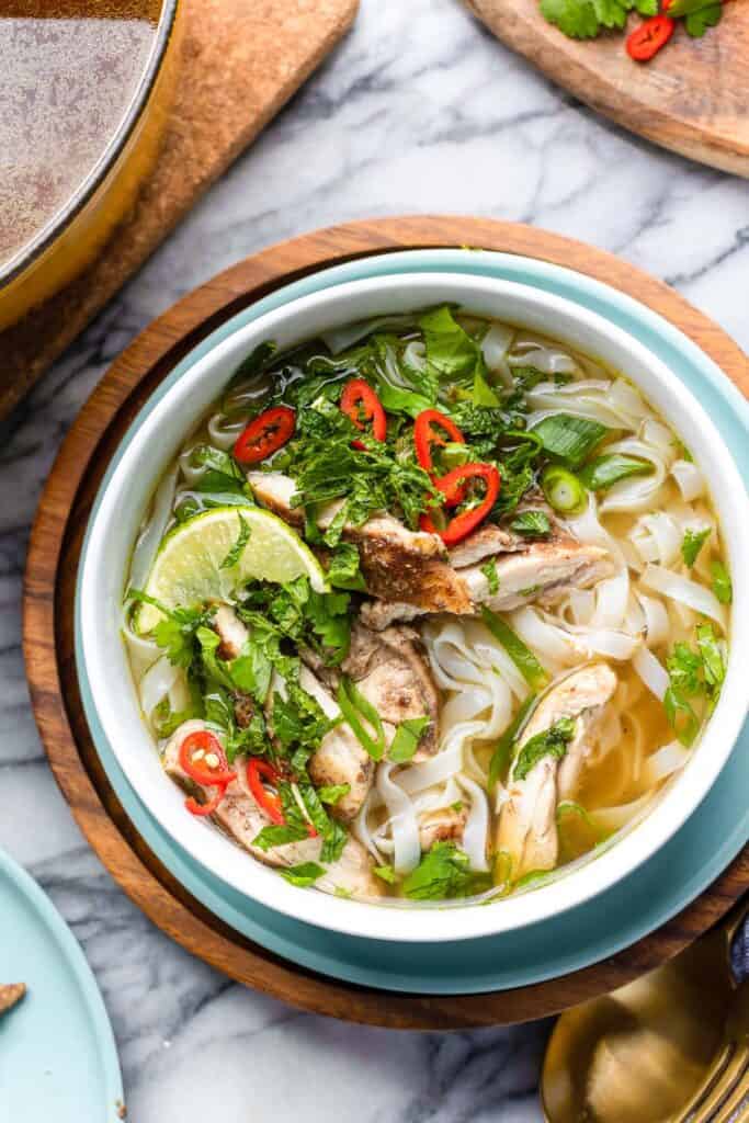 Five Spice Chicken Noodle Soup in a soup bowl topped with fresh herbs, chili slices and a lime wedge 