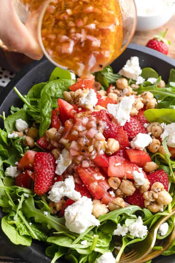 shallot vinaigrette pouring into a Strawberry Feta Salad with Candied Hazelnuts 