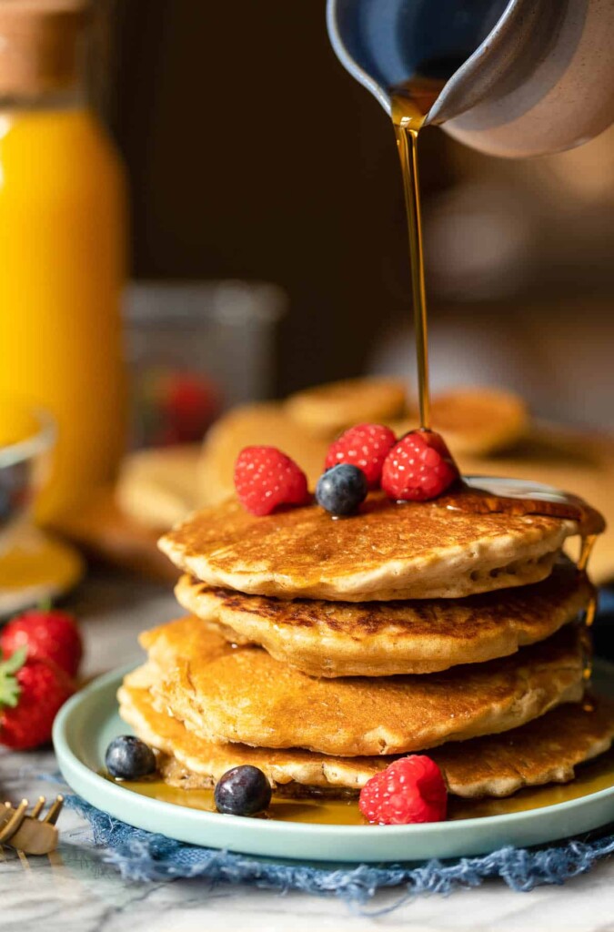 a stack of millet pancakes with maple syrup pouring over the top