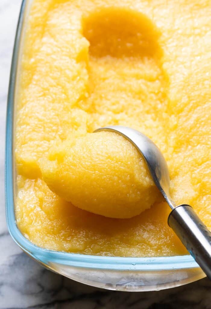Boozy Pineapple Mango Sorbet in a freezer safe container with an ice cream scoop 