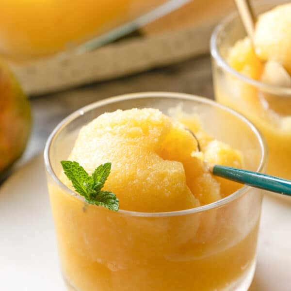 a small glass with Boozy Pineapple Mango Sorbet topped with a few fresh mint leaves