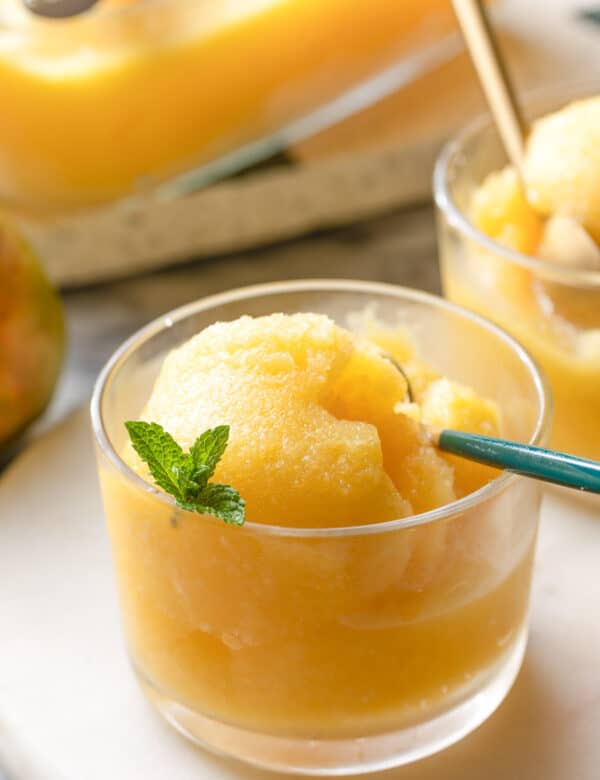 a small glass with Boozy Pineapple Mango Sorbet topped with a few fresh mint leaves