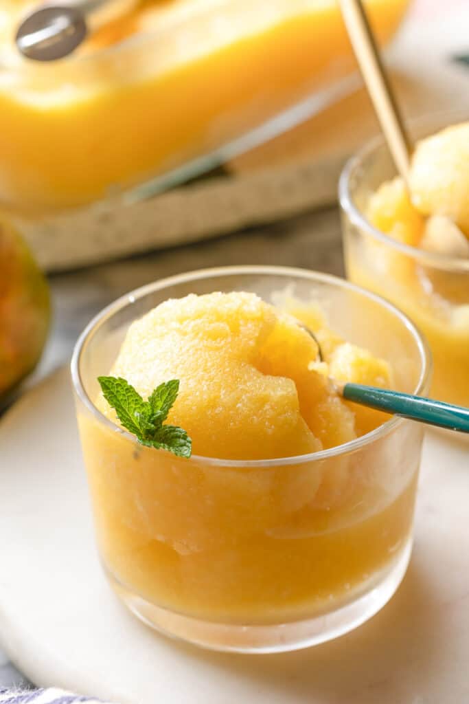 a small glass with Boozy Pineapple Mango Sorbet topped with a few fresh mint leaves