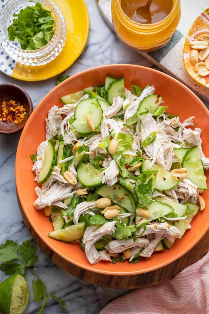 shredded chicken, sliced cucumnber, spring onions and cilantro with salted peanuts and red chili flakes mixed together in a bowl 