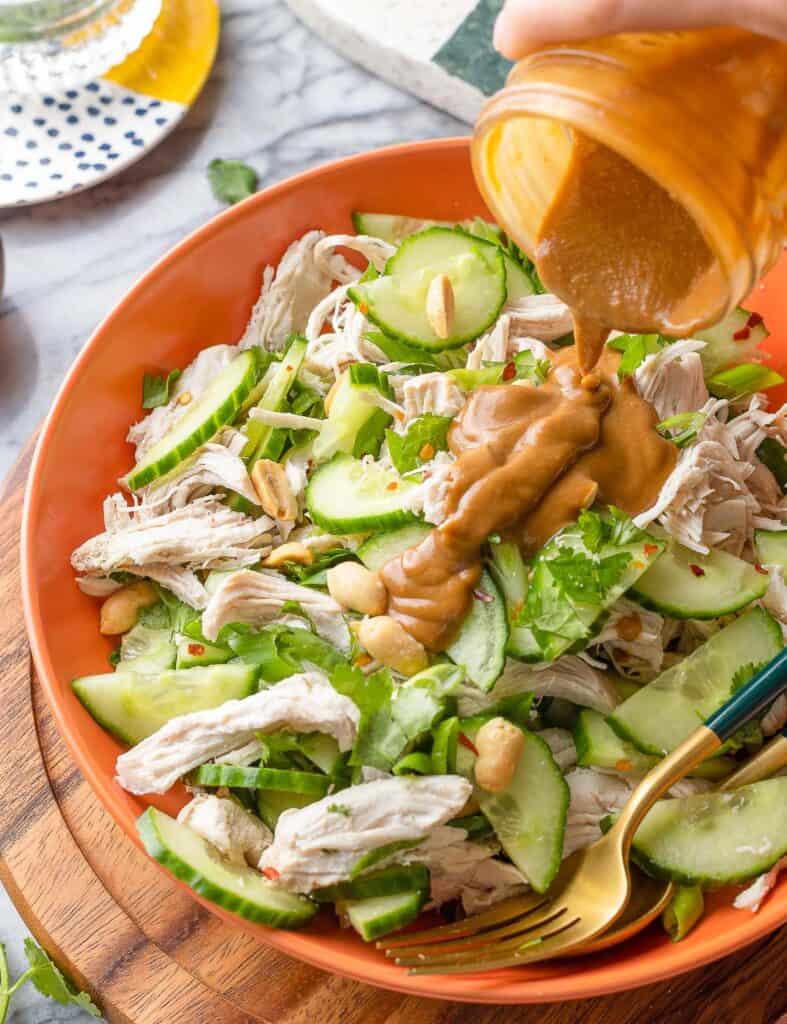 peanut lime dressing pouring over a bowl of cucumber chicken salad ingredients