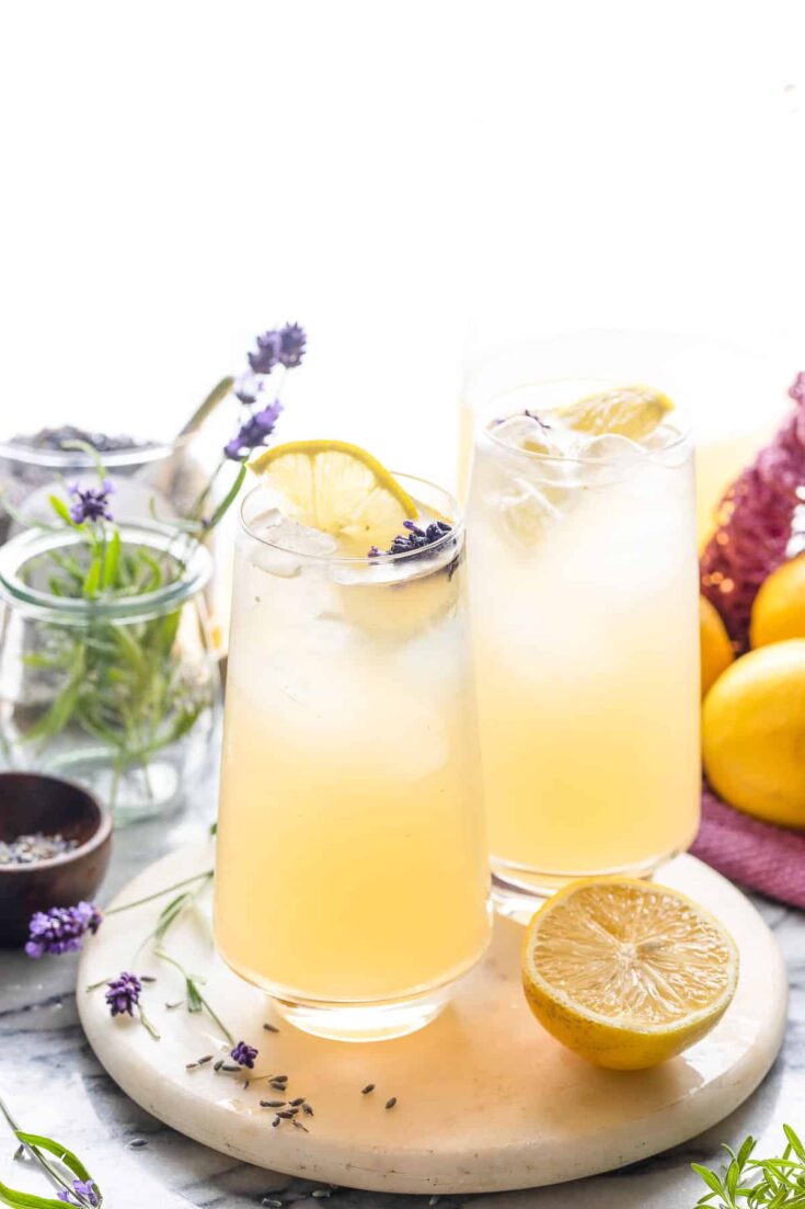 a couple of glasses of lavender lemonade with lemon slices and fresh lavender garnishing the glass