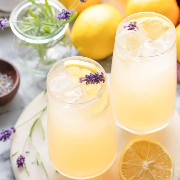 two glasses of lavender lemonade with lemon slices and fresh lavender buds garnishing the lgass