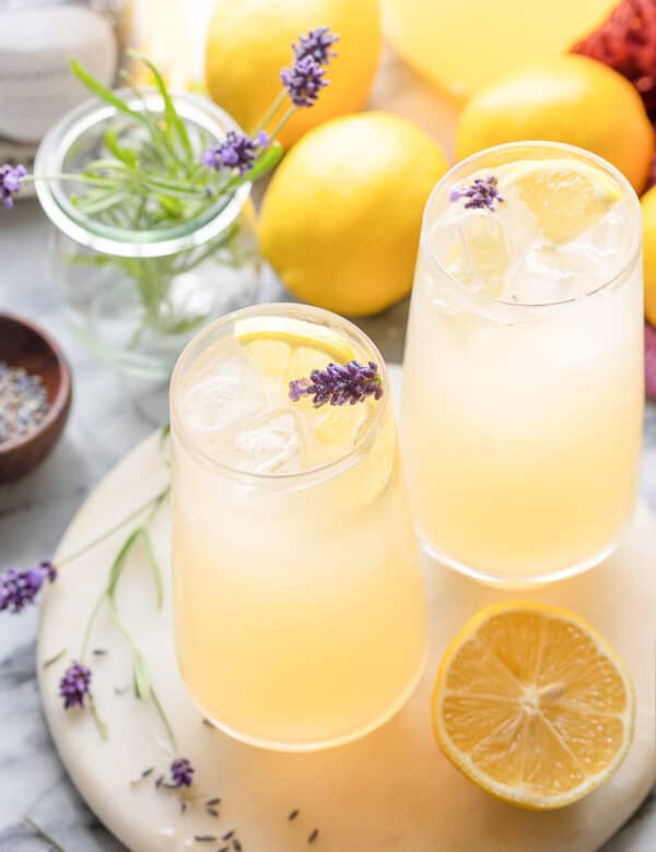 two glasses of lavender lemonade with lemon slices and fresh lavender buds garnishing the lgass