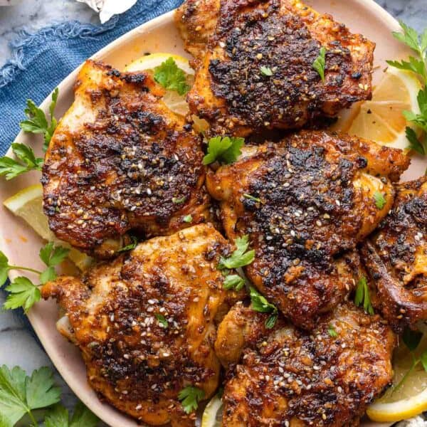 Baked Paprika & Za'atar Chicken Thighs on a plate with fresh parsley and lemon wedges
