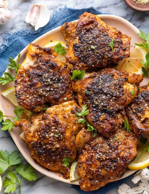 Baked Paprika & Za'atar Chicken Thighs on a plate with fresh parsley and lemon wedges