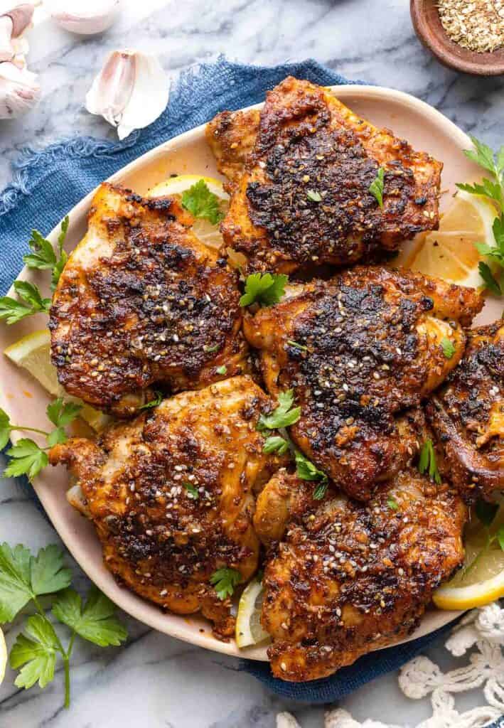 Baked Paprika & Za'atar Chicken Thighs on a plate with fresh parsley and lemon wedges