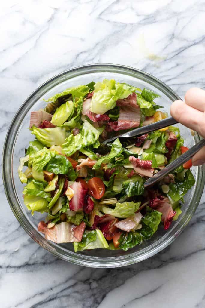 a pair of tongs mixing a BLT salad together in a bowl