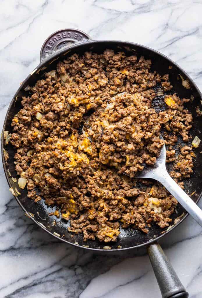 a cast iron skillet full of the meat and onion filling for a Chopped Cheese Sandwich