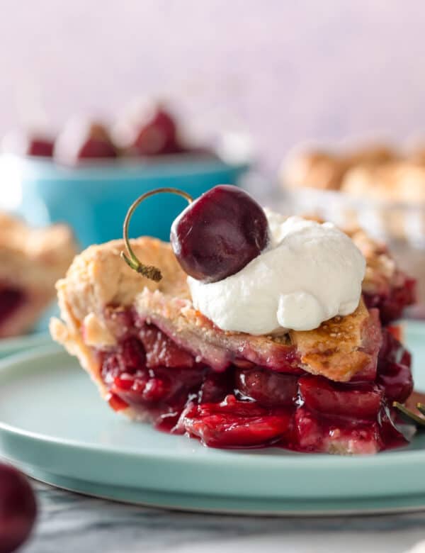 a slice of gluten free cherry pie on a plate topped with whipped cream and a fresh cherry
