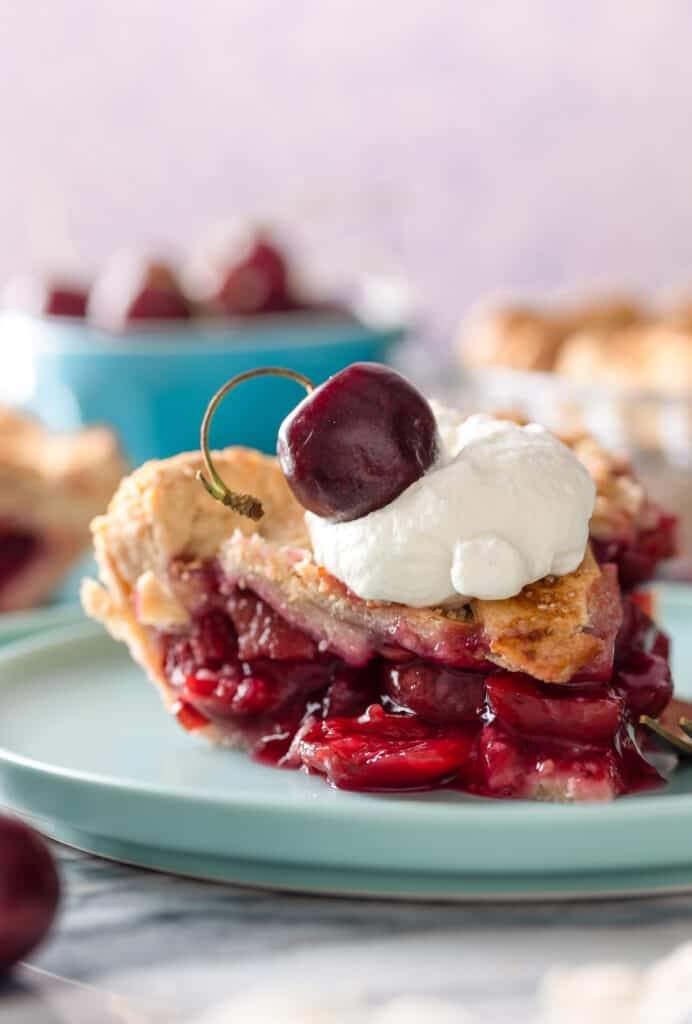 a slice of gluten free cherry pie on a plate topped with whipped cream and a fresh cherry