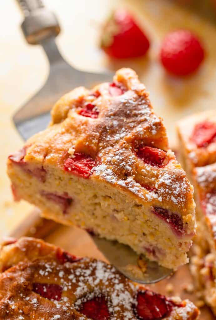 a slice of Strawberry Cornmeal Ricotta Cake help up by a cake knife