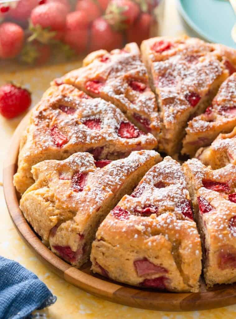 Strawberry Cornmeal Ricotta Cake cut into slices on a wooden plate with fresh strawberries in the back
