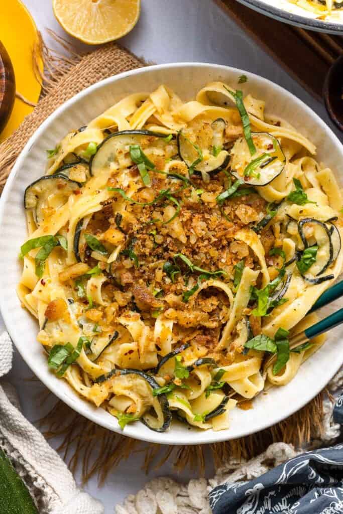 Lemon Zucchini Pasta in a serving dish with serving tongs topped with homemade crispy gluten free garlic chili breadcrumbs