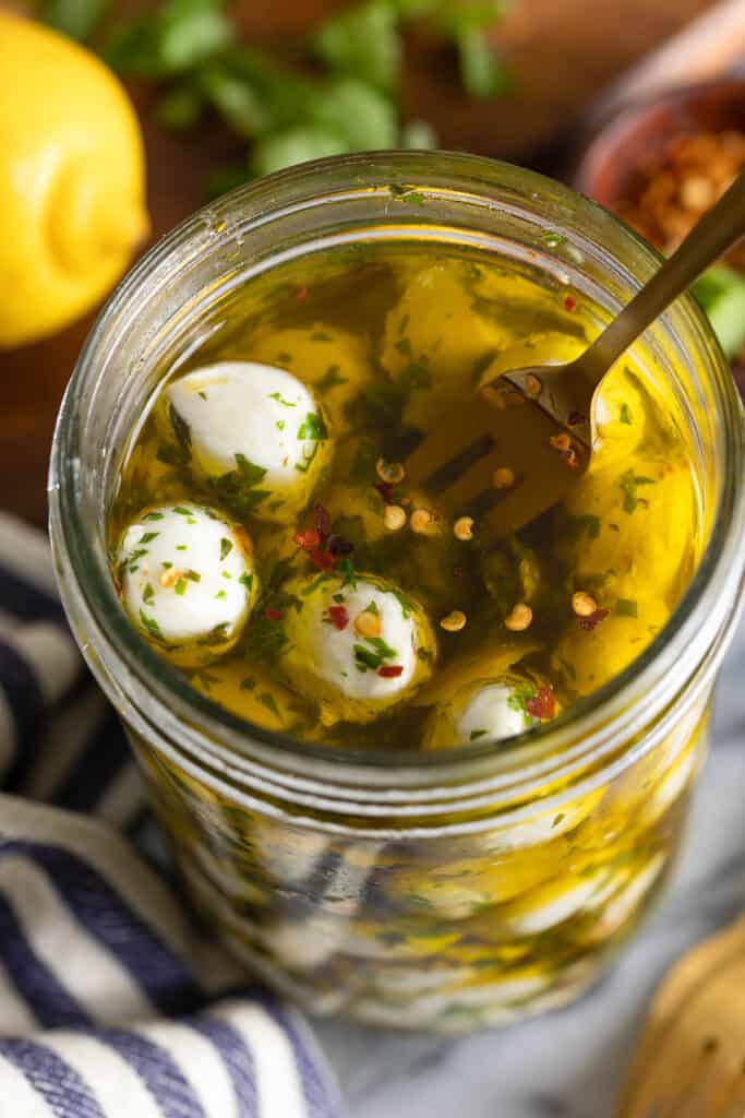 a jar full of marinated mozzarella balls with a fork poking in to a ball