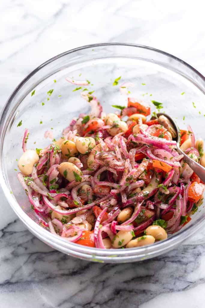 butter beans, sliced red onion, chopped tomatoes and parsley mixed together in a bowl with sumac and olive oil