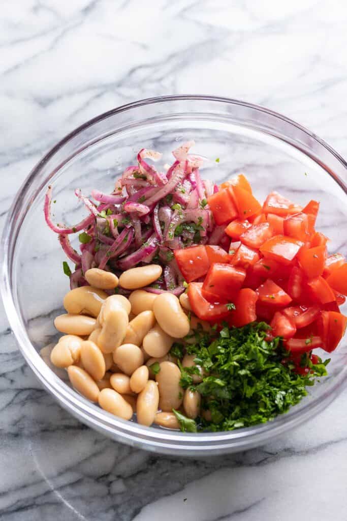 ingredients for a Piyaz (Turkish White Bean Salad) unmixed in a bowl: tomato, red onion, utter beans and parsley 