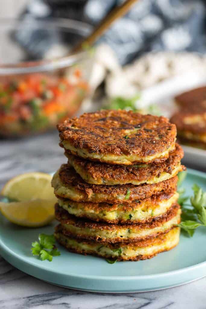 six  Ricotta Zucchini Fritters in a stack on a plate with lemon wedges and parsley