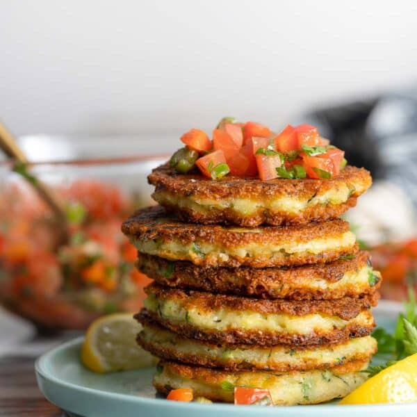 a stack of Ricotta Zucchini Fritters with a tomato caper salsa on top