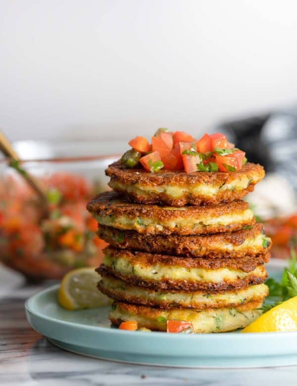 a stack of Ricotta Zucchini Fritters with a tomato caper salsa on top