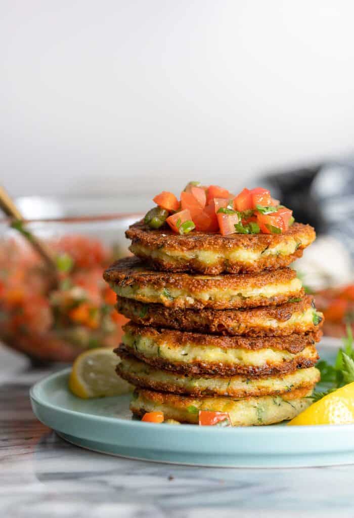 a stack of Ricotta Zucchini Fritters with a tomato caper salsa on top