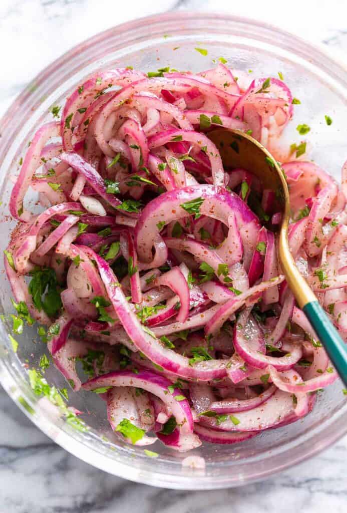 sumac onions and parsley marinating in a bowl with a mixing spoon