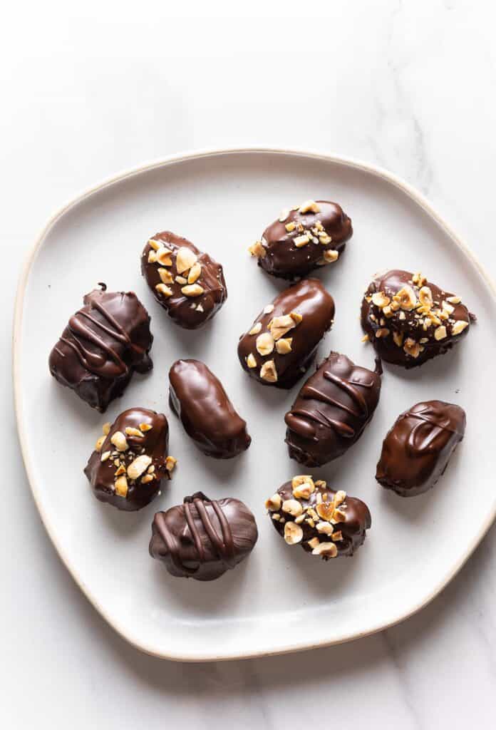 Chocolate Covered Dates on a plate: some dates are sprinkled with chopped peanuts and hazelnuts and some have only chocolate