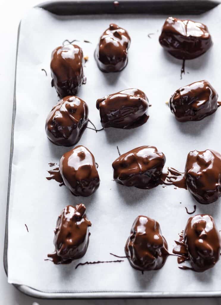 medjool dates covered in chocolate drying on a baking sheet lined with parchment paper